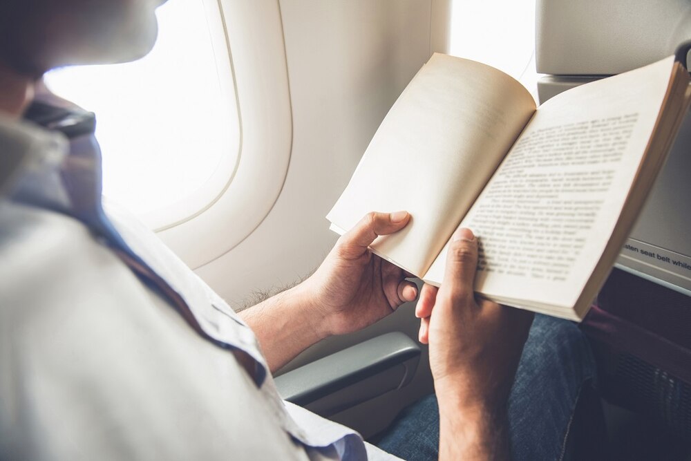 Male passenger killing time by reading book while traveling on the plane